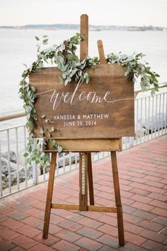 a welcome sign with greenery on it sitting in front of a body of water