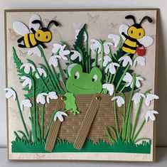 a card with some paper cut out of flowers and two bees in the back ground