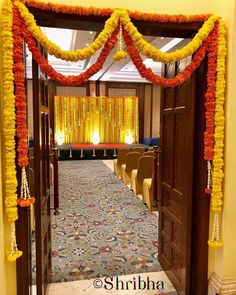 an entrance to a hall decorated with orange and yellow garlands, flowers and candles