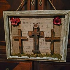 an old wooden frame with a cross and flowers hanging from the side on a wall