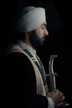 a man with a white turban holding a snake in his hands and looking down