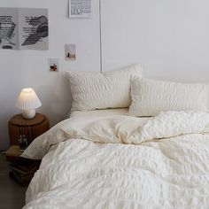 an unmade bed with white linens and pillows in a small bedroom area next to a night stand