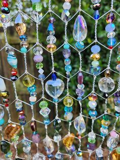 many different colored glass beads hanging from a wire mesh fence with trees in the background