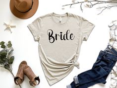 a t - shirt with the word bride on it next to some shoes and flowers