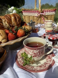 a cup of tea sits on a table with pastries and strawberries