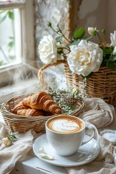 a cup of cappuccino sits on a saucer next to a basket of croissants