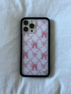 an iphone case with pink flowers on it sitting on a white sheet covered bedding