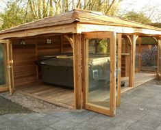 a wooden gazebo with a hot tub in the center and glass doors on both sides