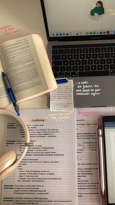 an open book sitting on top of a desk next to a laptop computer and headphones