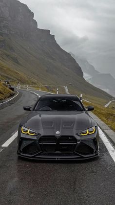 a black sports car driving down the road in front of a mountain range with cloudy skies