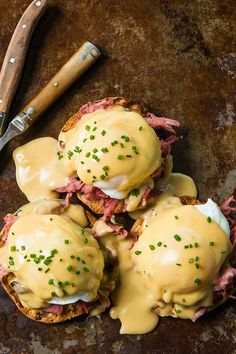 three open faced sandwiches covered in cheese on top of a table next to a knife