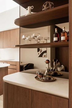 a kitchen with wooden shelves and white counter tops, filled with liquor bottles on top of it