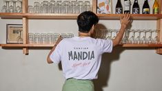 a man standing in front of shelves filled with liquor bottles and empty glassware on top of wooden shelves