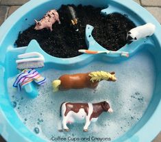 a blue bowl filled with toys and dirt in the shape of horses, cows, and giraffes