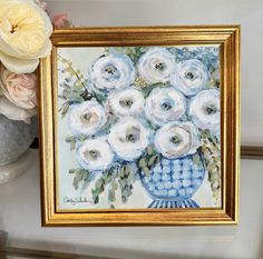 a painting of white flowers in a blue vase on a table next to a flower arrangement