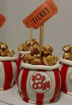 three red and white striped popcorn buckets with signs on them