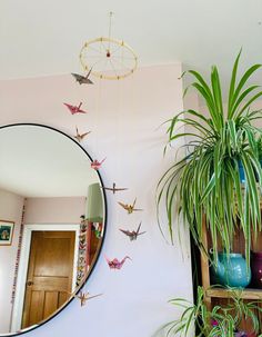 a mirror hanging on the wall next to a potted plant and bird mobiles