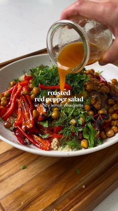 a person pouring dressing into a bowl filled with vegetables