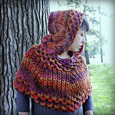 a woman standing next to a tree wearing a multicolored knitted shawl