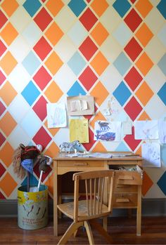 a desk with a chair and some papers on top of it in front of a colorful wall