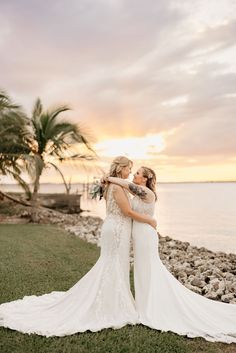 two brides embracing each other on the beach at sunset with palm trees in the background