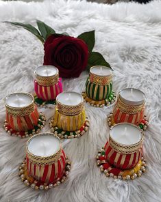 six candles are sitting next to a rose on a white furnishing with beads