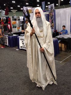 an old man dressed in white holding a staff and standing on the floor at a convention