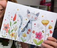 a woman holding up a card with an image of a cat and flowers on it