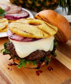 a cheeseburger with pineapple slices and onions on a wooden cutting board next to other food items