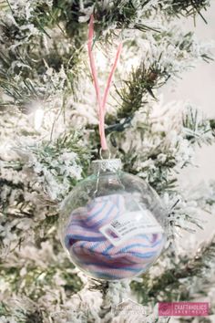 a glass ornament hanging from a christmas tree with snow on the branches and pink ribbon