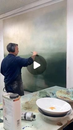 a man is painting on the wall in an art studio with his headphones on