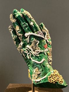 a green and white glove with gold decorations on it's palm, sitting on a wooden stand