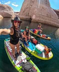 two women in bikinis are on paddle boats with dogs sitting on the front and behind them