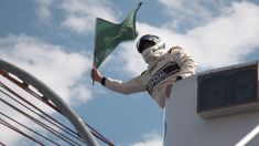 a man holding a green flag on top of a white building next to a metal railing