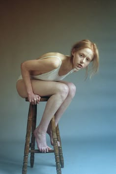 a woman sitting on top of a wooden stool with her legs crossed and one leg bent