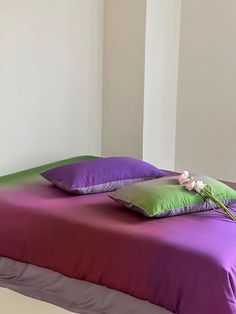 a bed with purple and green sheets, pillows and flowers on the pillowcases