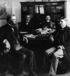 an old photo of four men sitting at a table in front of a world map