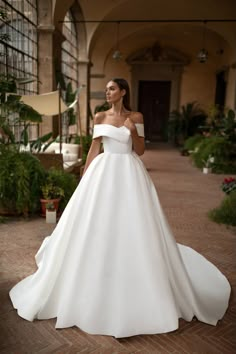 a woman in a white wedding dress standing on a brick walkway with her hand on her hip