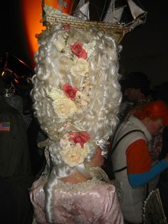 a woman dressed as a princess with white hair and flowers on her head is standing in front of a crowd