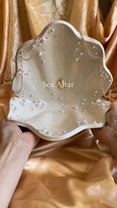 a person holding a white shell shaped object with pearls on it's side and the word sea attar written in gold