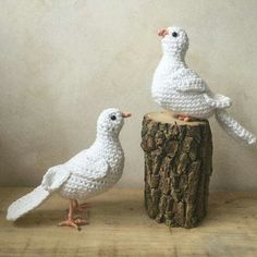 two white crocheted birds sitting on top of a tree stump next to each other