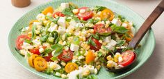 a green bowl filled with corn, tomatoes and lettuce next to a wooden spoon