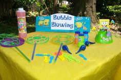 a yellow table topped with lots of toys and games on it's top, next to a sign that says bubble blowing