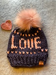 "All you need is Love Beanie, is set in soft pink words and subtle heart border, then framed in beautiful navy blue background. A warm winter toque that will get the looks as you set the tone letting people know \"Love\" is the answer to what we really need.  This hat is ready to ship and sized for circumference 21-22.5\" for average ladies and is approximately 9\" tall.  This soft squishy, fair isle knit toque is made with chunky acrylic yarn, in navy & pink. The top has a luxury faux fur Pom ties on and trimmed with a leather logo tag that says Hugs & Stitches on the outside and \"handmade with love\" on the inside! Pattern is adapted from the word beanie designs from Lady Jay Crochet. *hats should be hand washed paying careful attention to not submerge Pom, ans lay flat to dry. All shop Pink Knitted Hat As Gift, Pink Warm Hat As A Gift, Pink Warm Hat For Gift, Warm Pink Hat For Gift, Jay Crochet, Pink Winter Hat, Pink Words, Knit Toque, Love Is The Answer