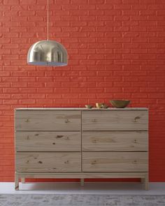 a wooden dresser sitting in front of a red brick wall with a light hanging from the ceiling