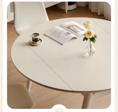 a white table topped with a vase filled with flowers and an open book on top of it