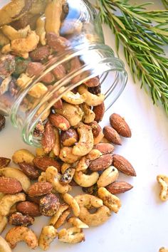 nuts spilling out of a jar on top of a white surface next to a sprig of rosemary