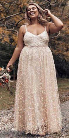 a woman in a long dress standing on a dirt road with her hands behind her head