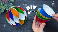 someone is holding two colorful cupcakes in front of a christmas tree with snowflakes on it