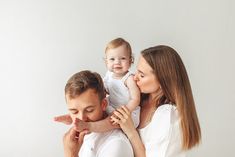 a man and woman holding a baby up to their face while they look at each other